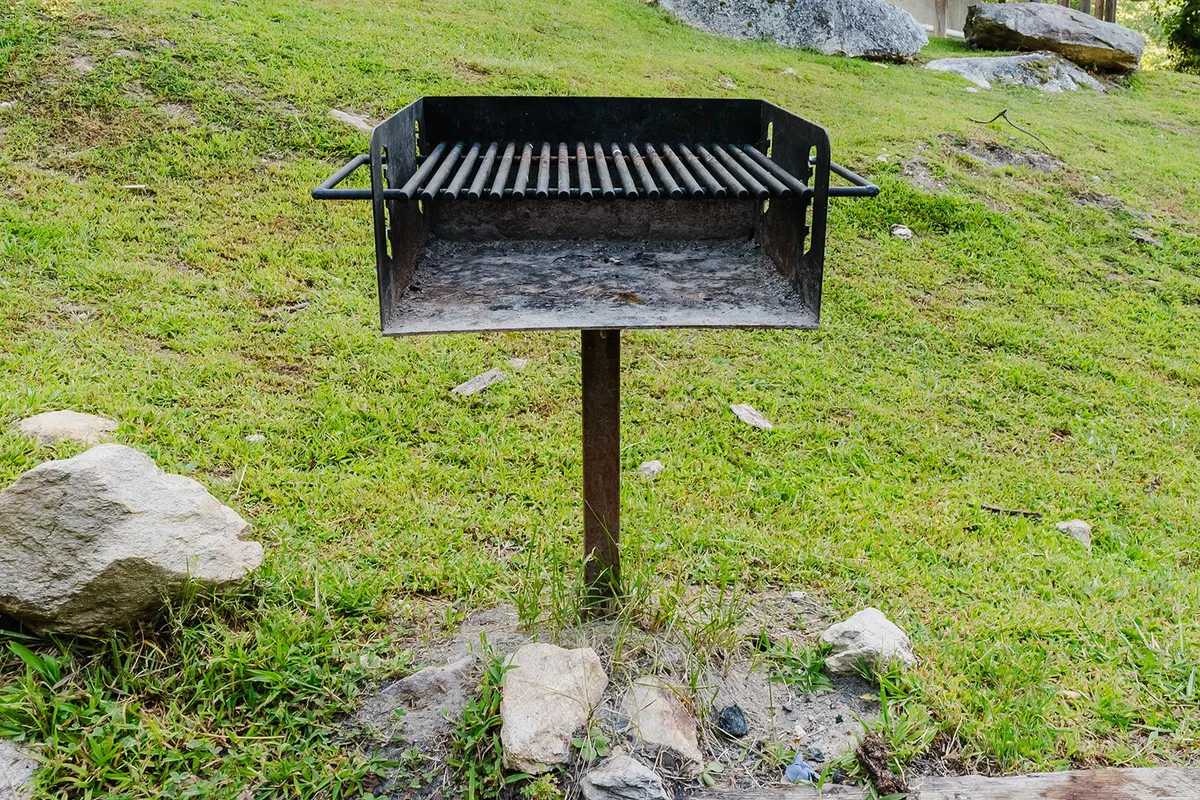 This exterior image focuses on the charcoal grill set amid lush grass and rocks, evoking the pleasure of outdoor cooking and communal meals after a day of adventure.