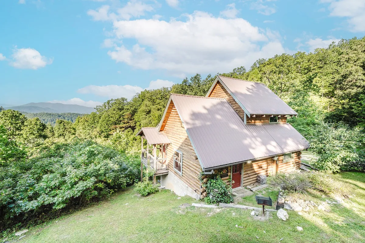 A wide shot of a log cabin nestled in lush natural surroundings, with a spacious deck area and the majestic Smoky Mountains in the background. The scene includes outdoor furniture, inviting families to relax and enjoy the scenery after a day of adventure.