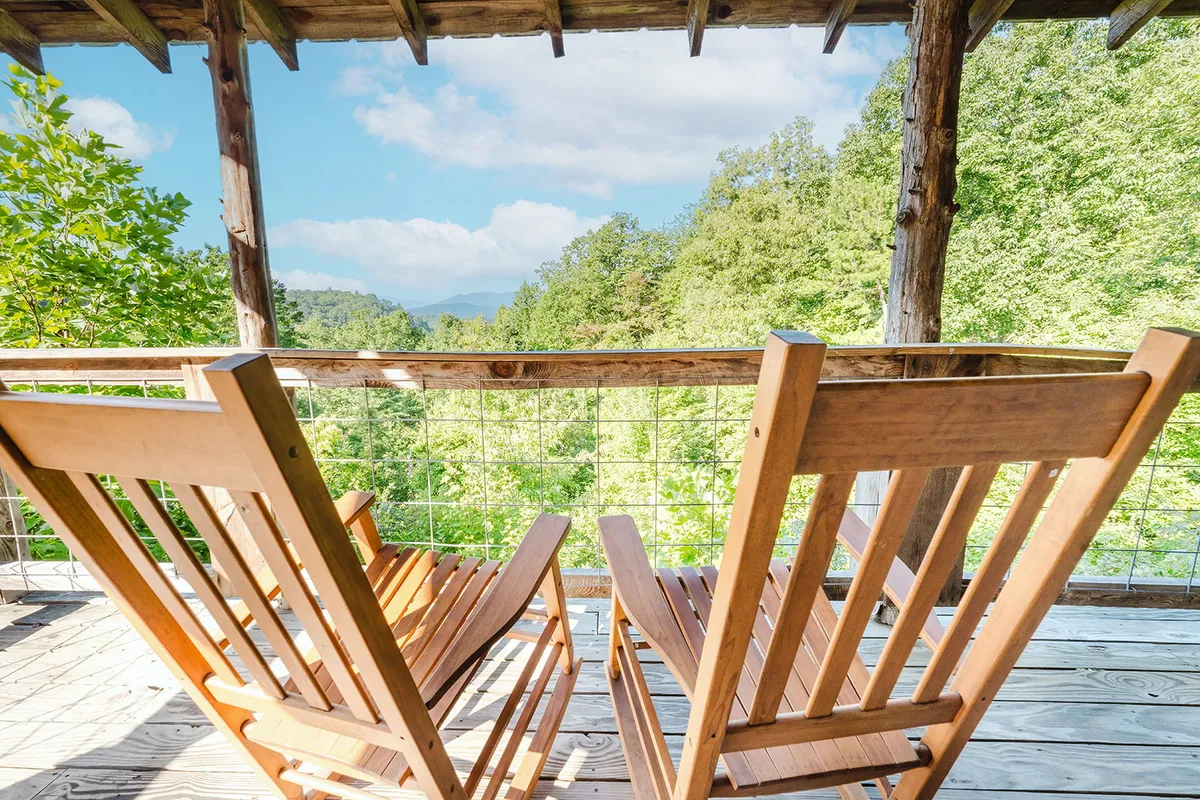 A serene porch scene featuring classic wooden rocking chairs and a view of lush greenery and open sky. The porch is an ideal spot for morning coffee, watching wildlife, or sharing stories with family after exploring local attractions.