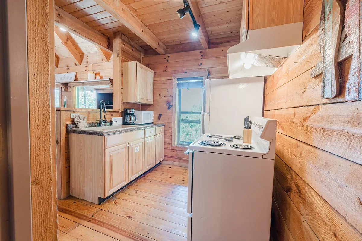 This image presents a warm, rustic kitchen with wooden cabinetry, a white stove, a large window allowing natural light to filter in, and a granite countertop. The scene feels inviting and captures the essence of cooking together as a group or family. Visible kitchen tools and surfaces support the sense of a fully equipped cooking space.