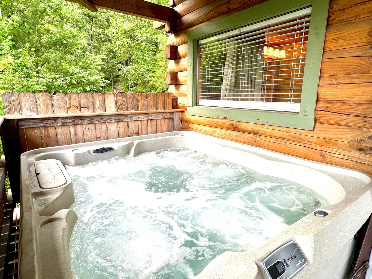 A tranquil outdoor hot tub surrounded by natural greenery and a rustic wooden fence, inviting guests to unwind. The setting suggests relaxation and socializing, with views of the surrounding forest visible from the tub.
