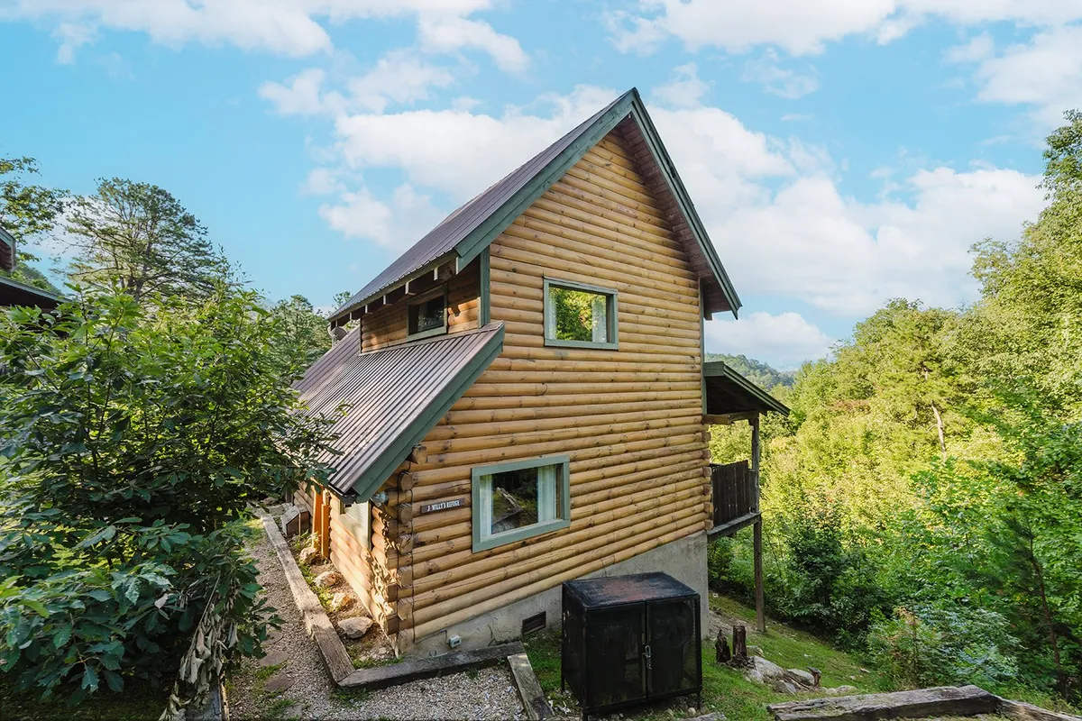 This image features a picturesque log cabin surrounded by vibrant greenery and set beneath a bright blue sky. The cabin’s exterior hints at inviting warmth within, while the surrounding natural landscape invites exploration and relaxation in the great outdoors.